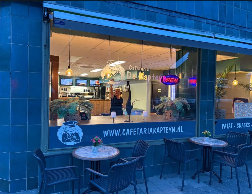 De etalage van Cafetaria de Kapteyn met tafeltjes op de stoep